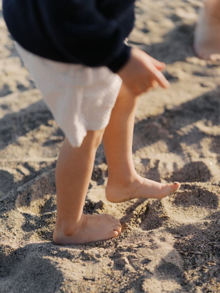 A young boys sandy feet walking through the sand in golden hour light.