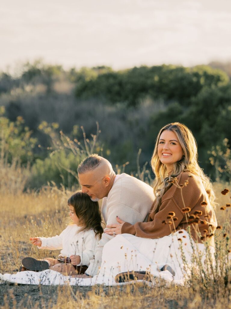Family of three sitting on a white blanket in golden grass during a sunset photo session in Thousand Oaks