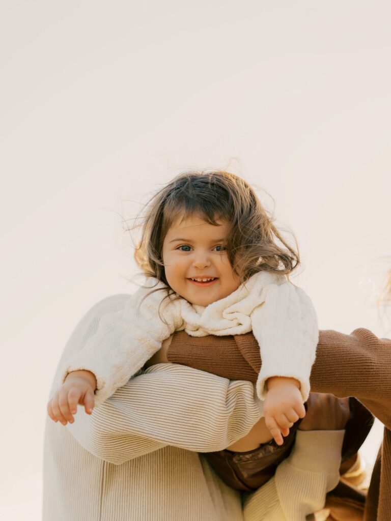 Smiling toddler girl lifted in the air by her parents against a soft golden sky in Thousand Oaks